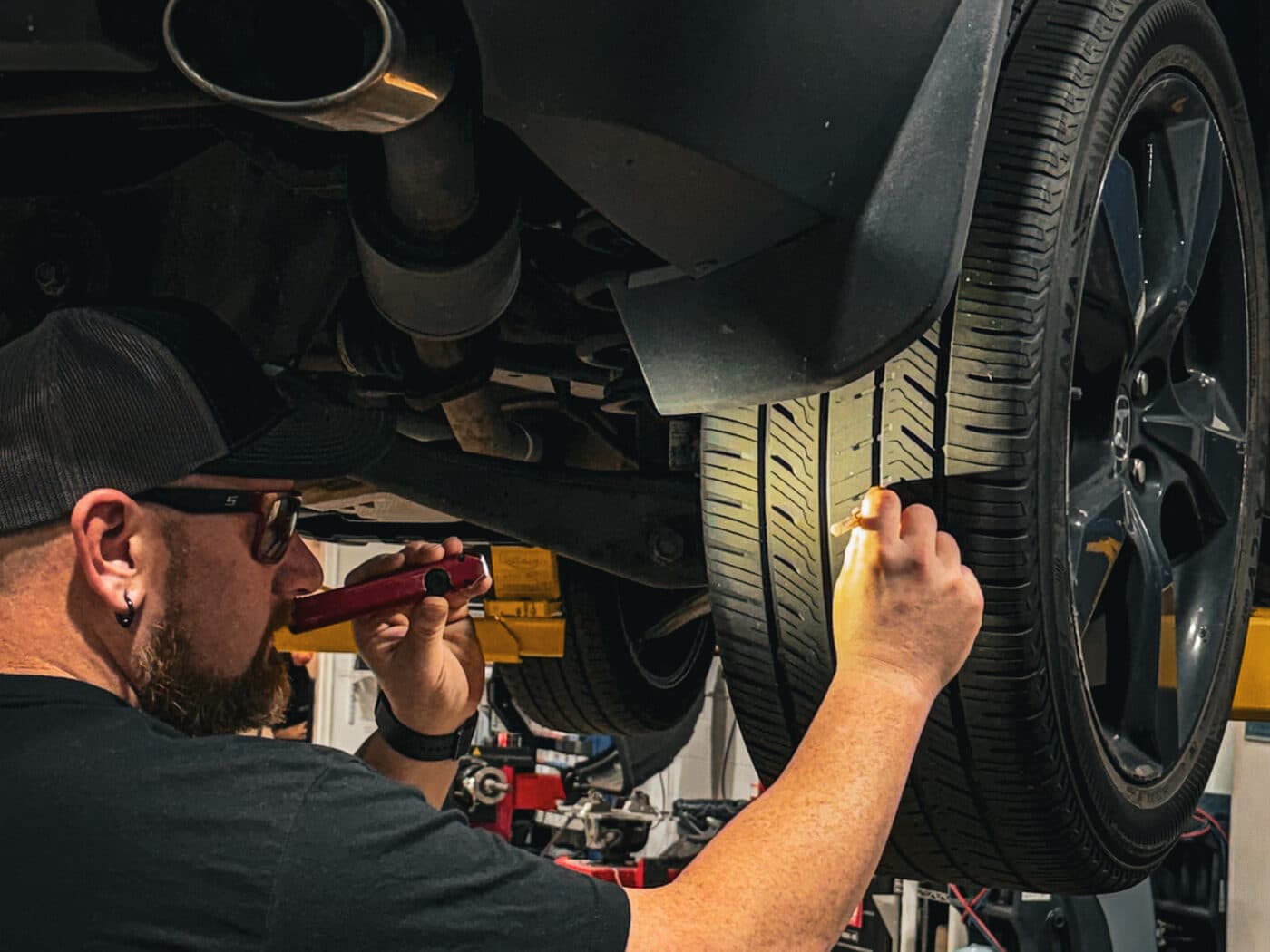 A Handled automotive technician checking the underside of a raised car with a flashlight
