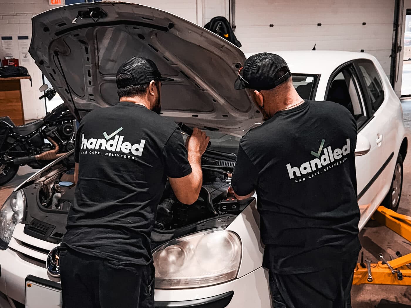 Two Handled automotive technicians working together under the hood of a car