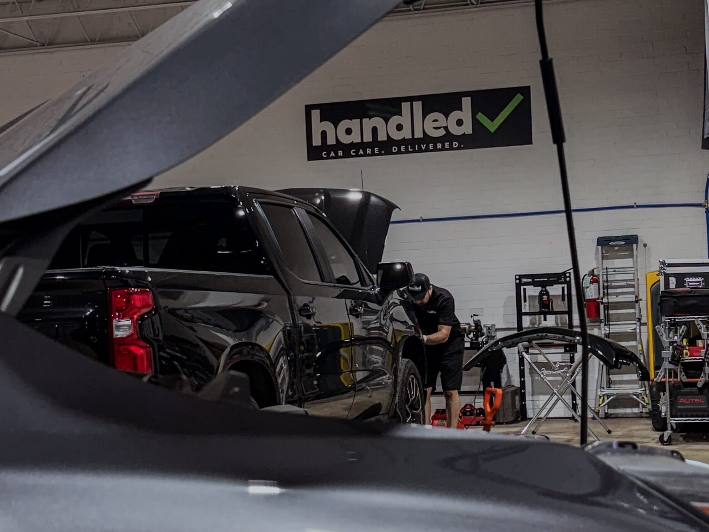 A Handled automotive technician at work on a pickup truck beneath the Handled sign