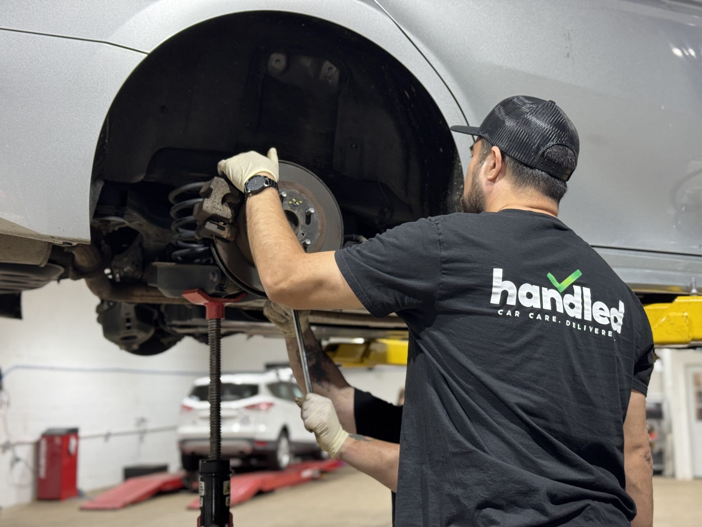 A Handled automotive technician performing brake service on a lifted car